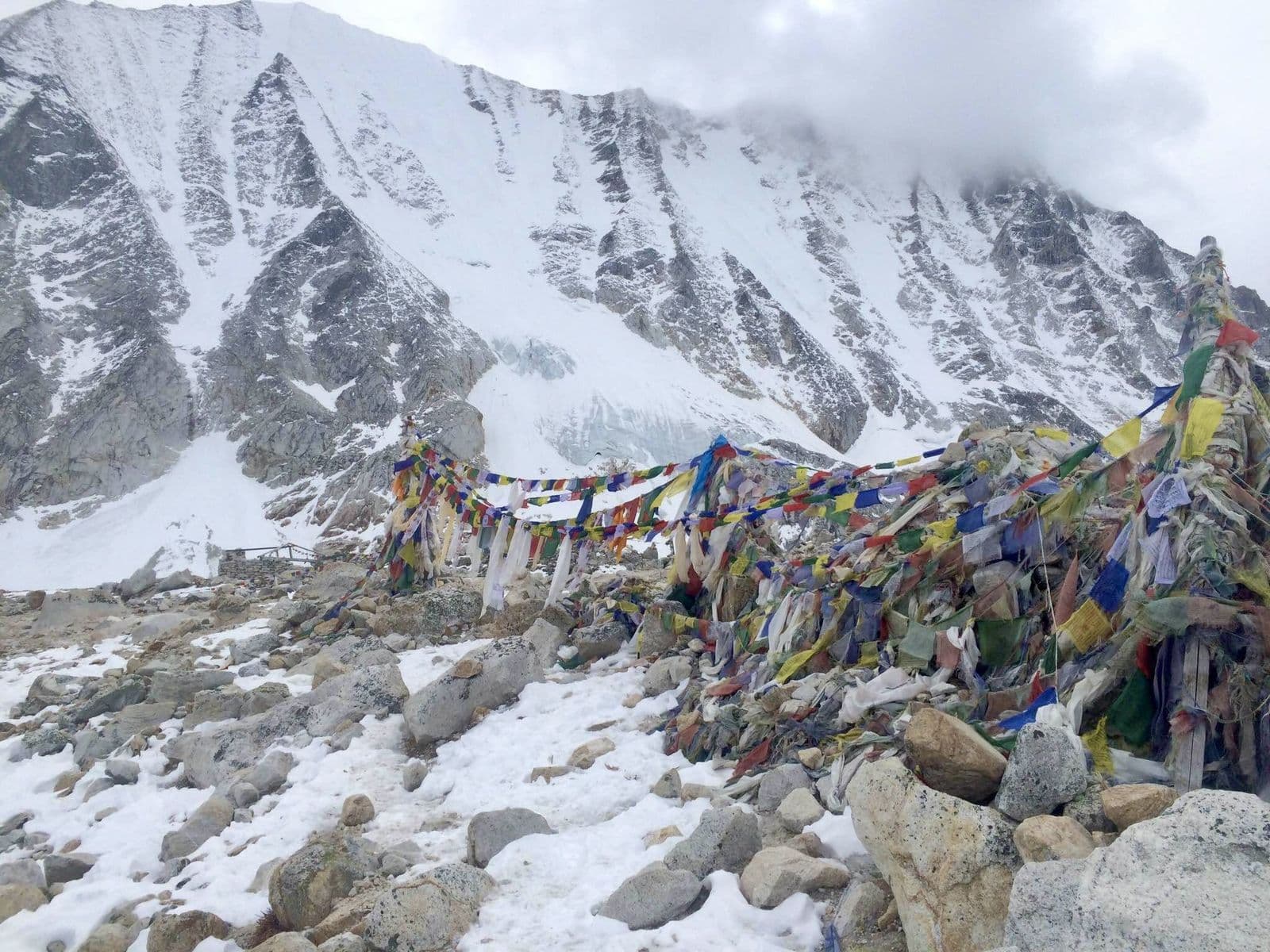 Prayer flags across a snowy moraine below a Himalayan wall