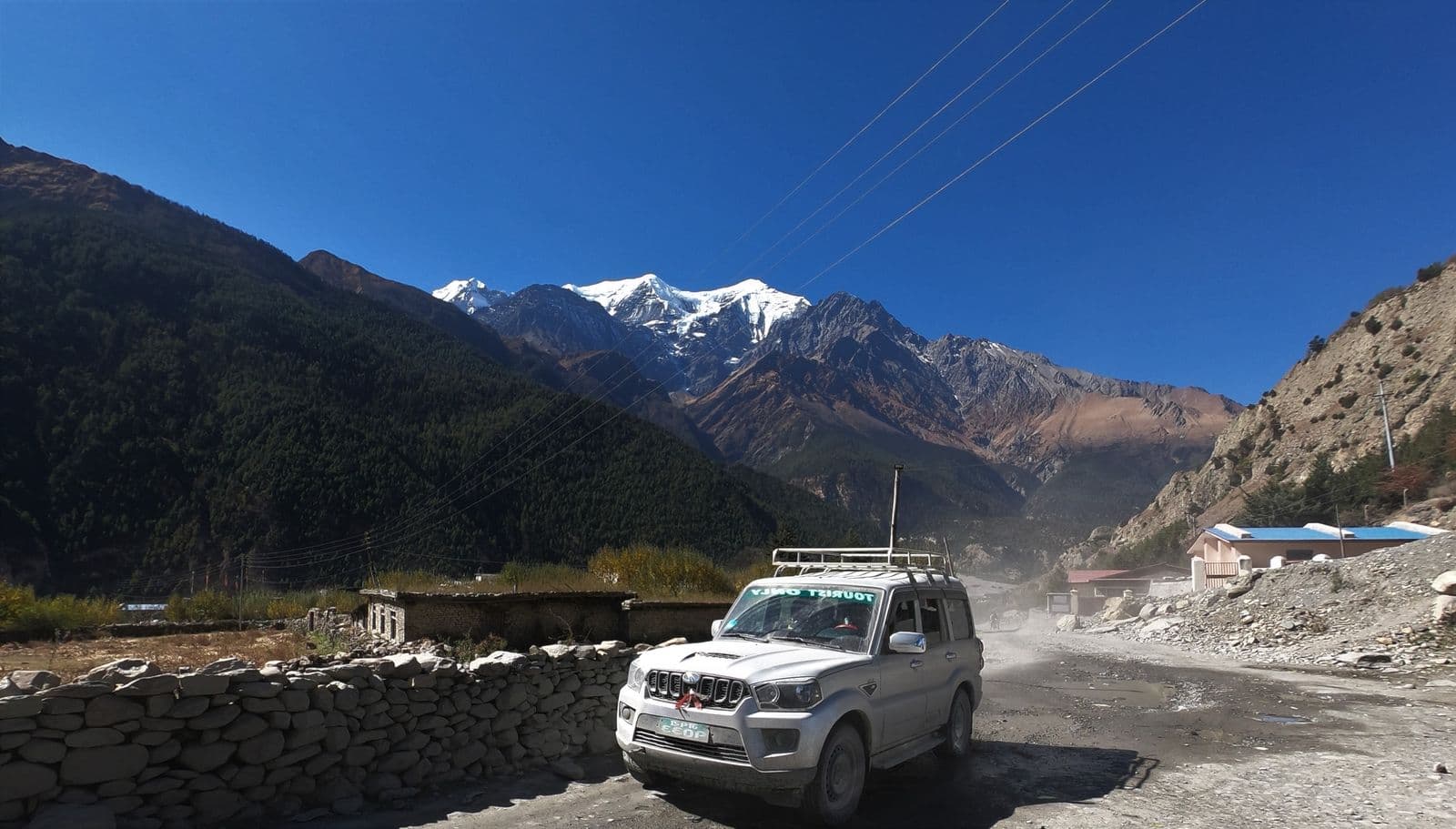 Jeep on a mountain road below snowy peaks