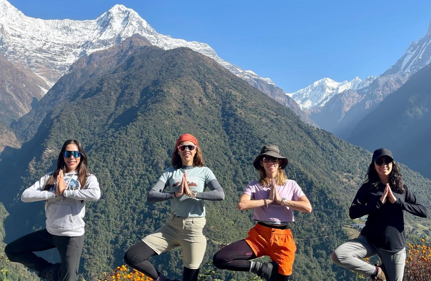 Trekkers in tree pose with Himalayan peaks behind