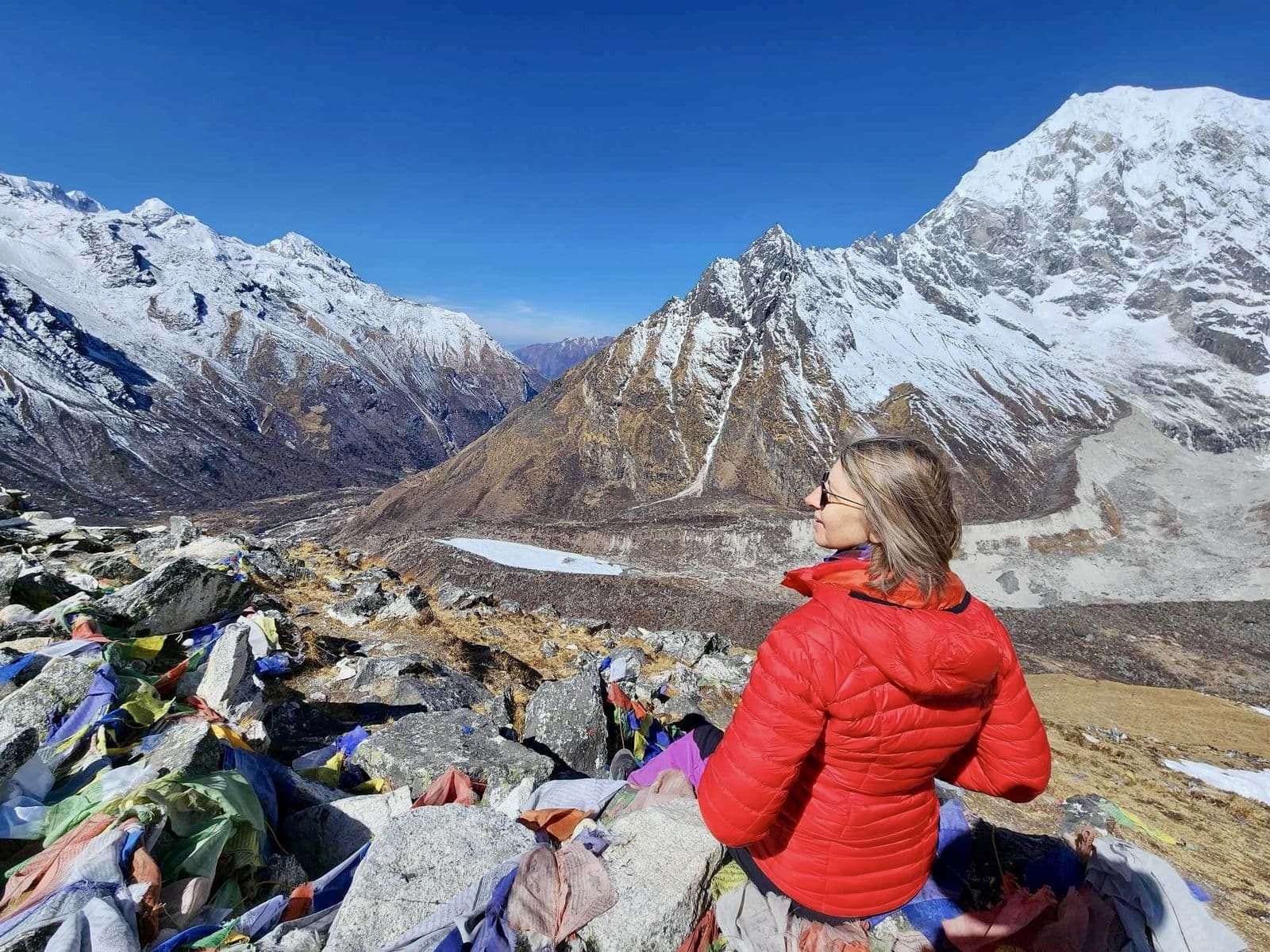 Trekker in a red jacket among prayer flags at a high pass