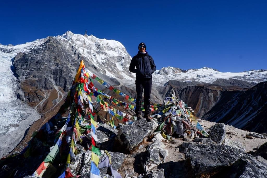 Trekker standing on a rock with prayer flags and glaciers